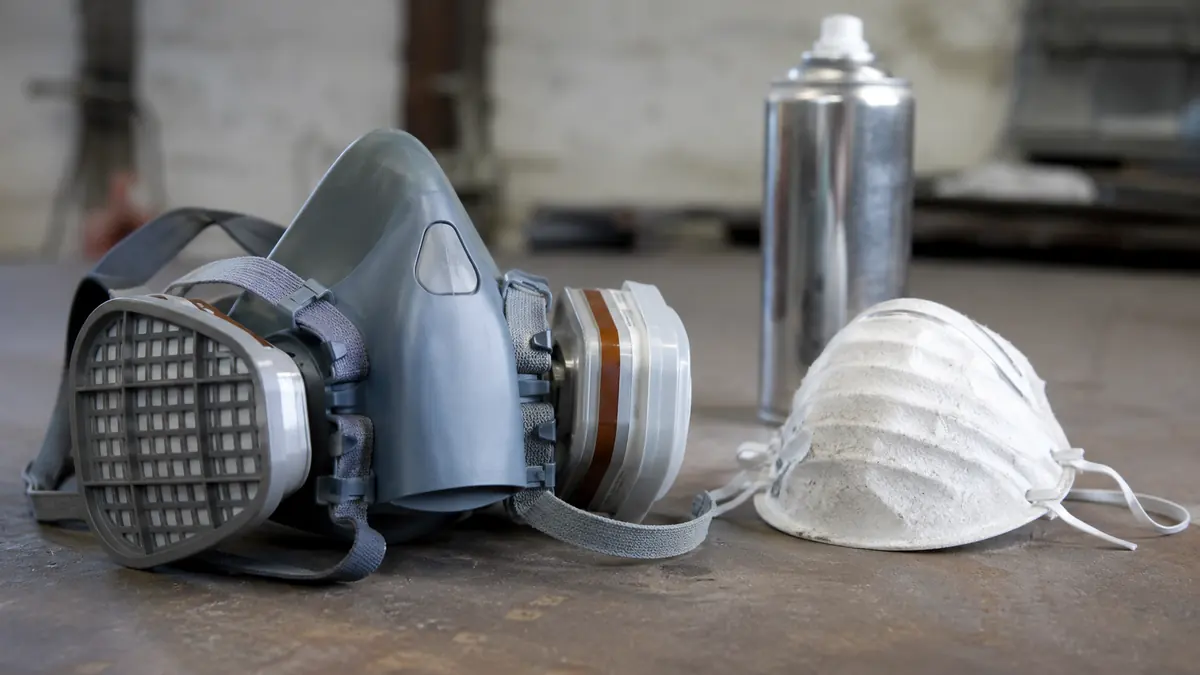 Halbmaske mit A2P3-Filter und Chromlack-Spraydose auf einer Werkbank, im Vergleich zu einer ungeeigneten FFP2-Staubmaske